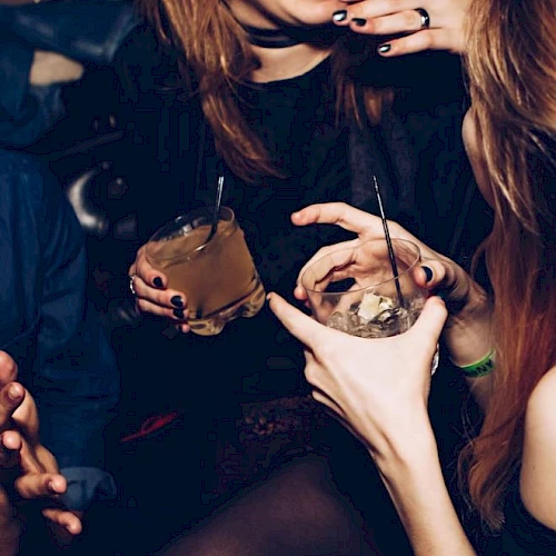 People are sitting and holding drinks, with one person laughing and others engaging in conversation in a social setting.