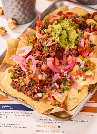 A tray of nachos topped with ground beef, guacamole, diced onions, tomatoes, and jalape&ntilde;os.