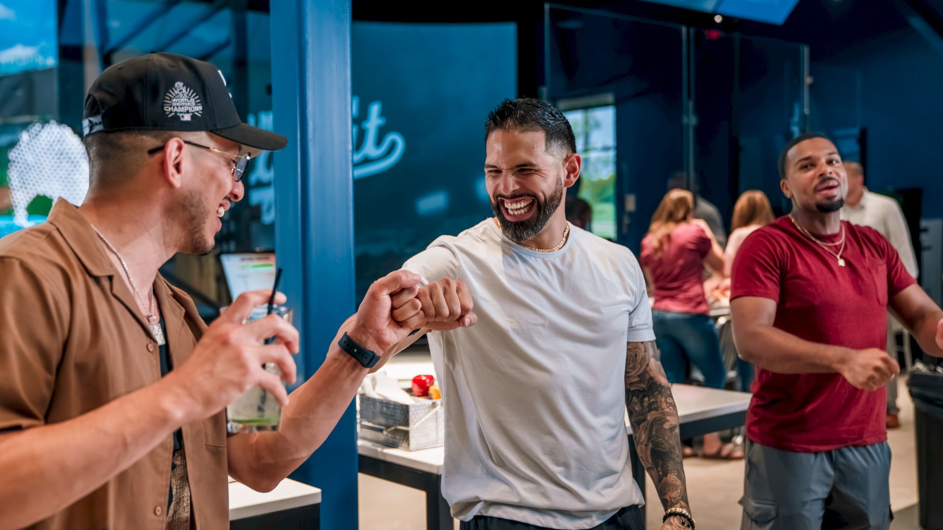 Three men are indoors having fun; two exchange a fist bump while the third smiles.