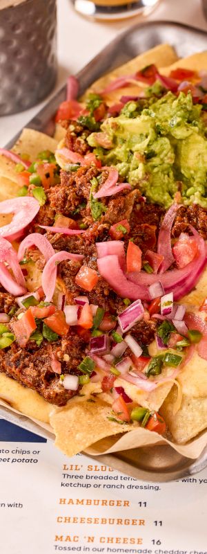 A tray of nachos topped with ground meat, guacamole, cheese, diced tomatoes, pickled onions, and jalape&ntilde;os.
