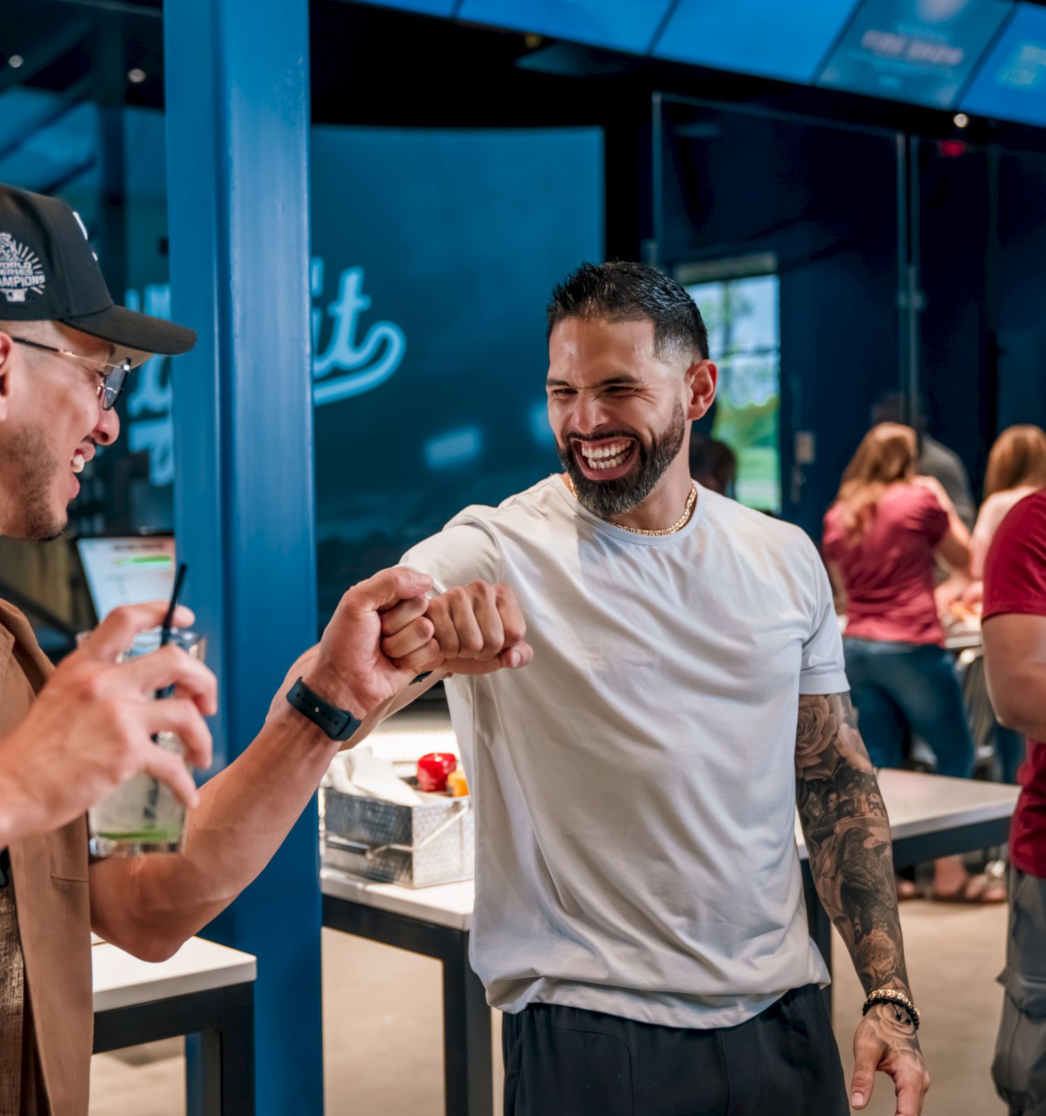In a blue-lit event lounge, two men share a celebratory fist bump while others chat and watch nearby.