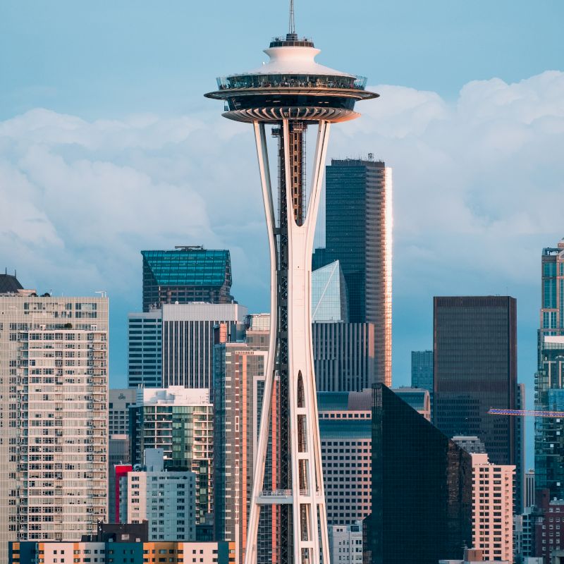 The image shows the Space Needle in Seattle, with surrounding skyscrapers against a cloudy sky in the background.
